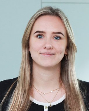 Eine junge Frau mit langen, blonden Haaren und einem freundlichen Gesichtsausdruck trägt ein schwarzes Oberteil mit weißem Kragen.