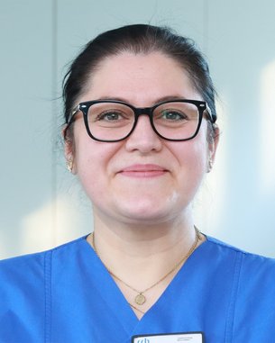 Eine Person mit Brille und blauer Arbeitskleidung lächelt freundlich in die Kamera.